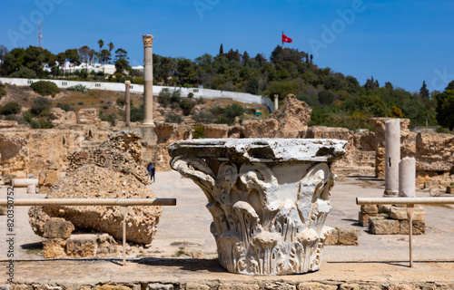 Detailed view of preserved decorative capital of Corinthian column against sunlit stone ruins of ancient Roman Baths complex of Antoninus in Carthage at Tunisian archaeological site