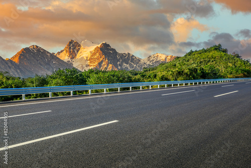 Asphalt highway road and green forest with snow mountain nature landscape at sunset