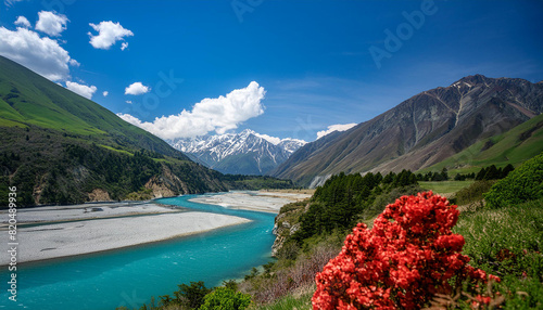 Create a beautiful landscape of a river valley flowing through green hills and snow-capped mountains in the distance. The river is a clear blue, winding between rocky cliffs and lush meadows.