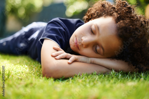 Boy, child and sleeping on lawn in garden of home for resting, exhausted and tired with dreaming in nature. Kid, fatigue and nap on grass in backyard with comfort, peace or relax for wellness outdoor