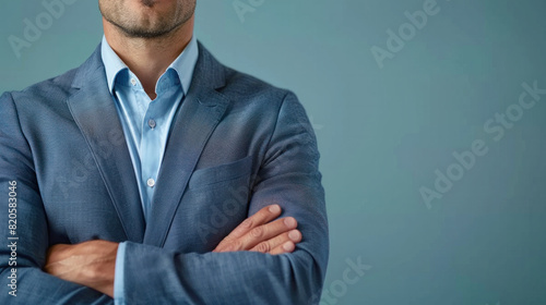 A man in a blue suit is standing with his arms crossed. The suit is wrinkled and has a watermark on it. The man's expression is serious and focused