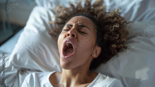 A close-up of a person yawning while working in bed, eyelids drooping