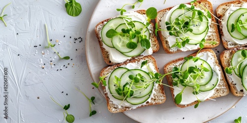 Fresh open-faced sandwiches topped with cucumber, cream cheese, and microgreens, served on a rustic white background