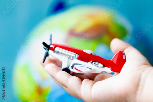 Child's hand holding a toy airplane with a propeller in his palm. Red toy plane in front of world model background. Aviation.