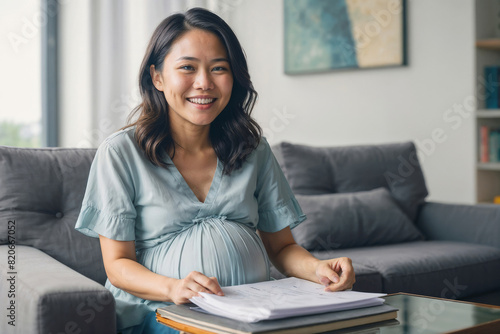Portrait of happy pregnant Asian woman is sitting on the sofa in the living room, holding a document with good news in her hand. Good news, excellent pregnancy tests, bank loan approval
