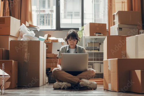 A young person sitting cross-legged on the floor, using a laptop, surrounded by moving boxes in a room. A moving or unpacking process. AI generative