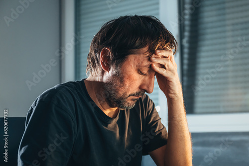 Lonely and depressed adult man with eyes closed at home. Unshaven male sad and unhappy. Mental health and regret concept.