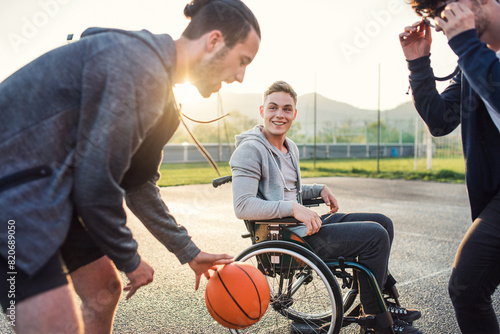 Disabled young man in a wheelchair playing basketball with his friends. Teamwrok and male friendship.