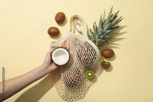 Set of tropical fruit in bag and hand on beige background, top view