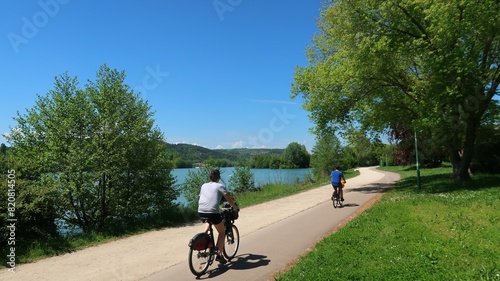 Cyclotourisme au bord du lac du chanoine Kir à Dijon, en Côte d’Or / Bourgogne, paysage de nature avec deux cyclistes roulant sur une piste cyclable au bord de l'eau (France)