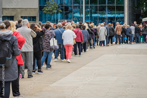 Long queue on street, waiting patiently. Public crowd. Women and men. Consumerism concept