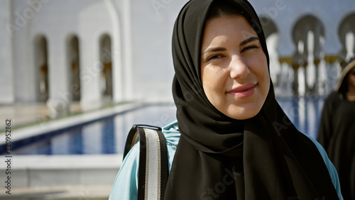A smiling young adult hispanic woman in a hijab at an islamic mosque in abu dhabi, showing beauty and tourism.