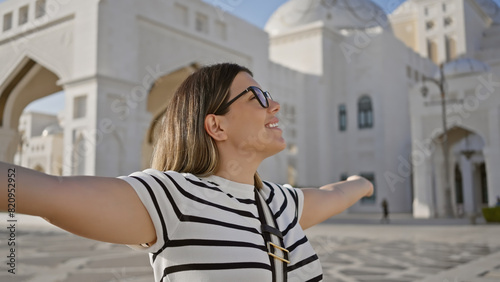 Happy woman with arms open in front of the grand qasr al watan in abu dhabi, embodying travel and joy.