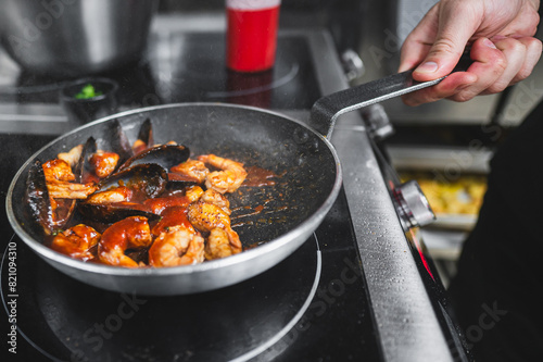 Close-up of a hand holding a sizzling frying pan with seafood