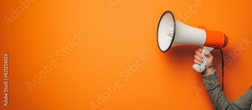 A woman's hand holds a white and orange hand-held megaphone on an orange background. Concept of advertising, communication. Banner.