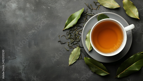 Cup of freshly brewed tea with bay leaves on grey table, top view