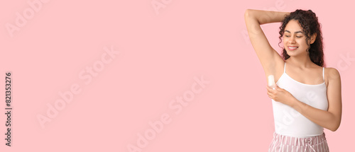 Beautiful young African-American woman applying deodorant on pink background with space for text