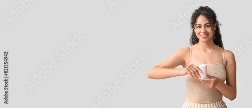Beautiful young African-American woman holding deodorant on light background with space for text