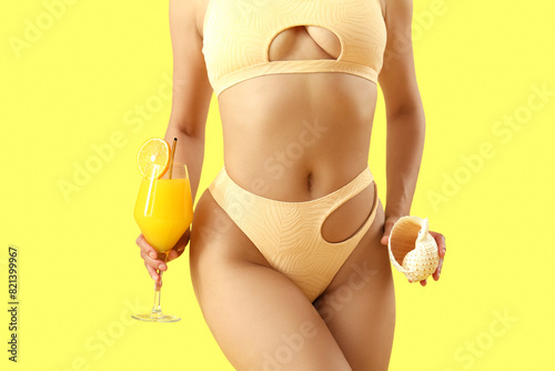 Attractive young woman in swimsuit with cocktail and seashell on yellow background, closeup