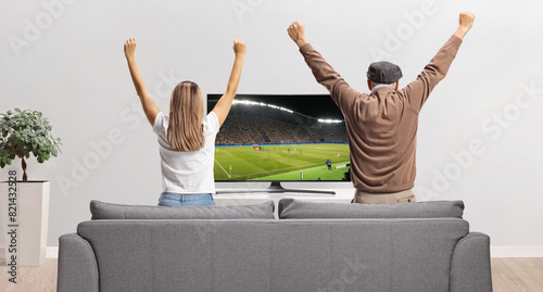 Rear view shot of an elderly man and a young woman watching a football match on tv