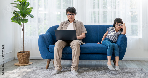 Senior Asian man relaxing using laptop computer working video conference meeting chat with bored lonely depressed little girl daughter. Work from home sme, freelancer single father concept