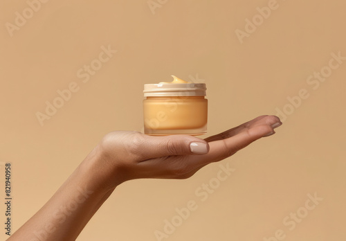 Womans hand with a jar of anti ageing cosmetics moisturiser cream against a beige tone background