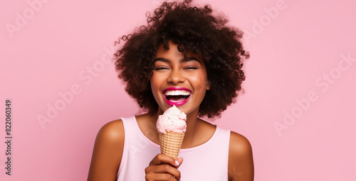 Summer portrait of happy cheerful young African woman eating ice cream cone, curly hair on pink