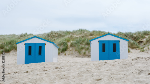 Two charming beach huts with vibrant blue doors stand out amidst the sandy shores of Texel, inviting visitors to relax and enjoy the seaside views. De Koog beach Texel