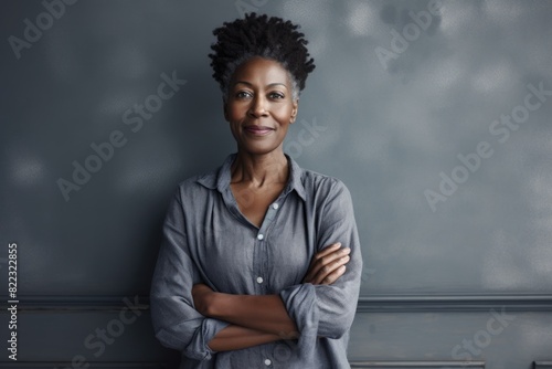 Portrait of a satisfied afro-american woman in her 50s with arms crossed in front of bare monochromatic room