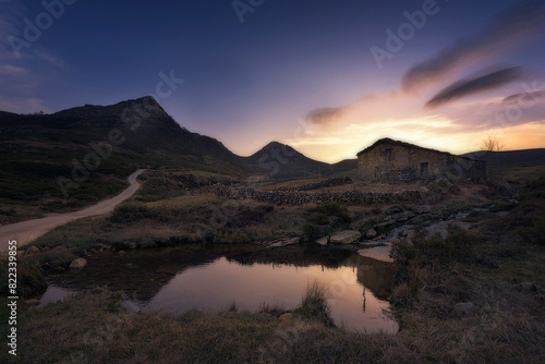 warm sunrise at the Pardo waterfall, in the mountain pass of Estacas de Trueba, Burgos, with a small pond in the foreground and a pasiega cabin between mountains