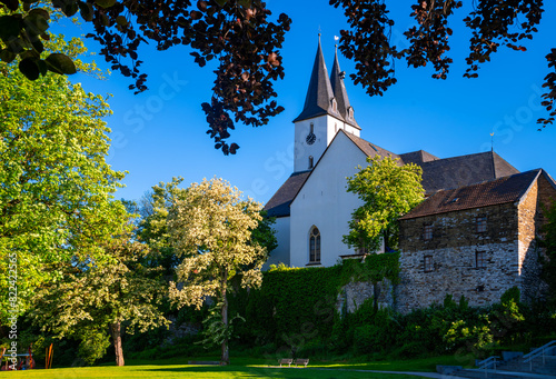 Protestant Church “Oberste Stadtkirche“ in Iserlohn, Sauerland Germany with twin bell towers, white facade, historical medieval library building and flowering trees on a sunny spring morning in May.