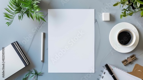 Blank paper, pen, coffee, and office supplies on a gray desk with green plants. Flat lay composition with copy space for design and print