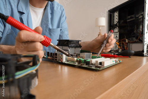 Male technician with soldering iron repairing computer board at table in service center, closeup