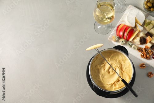 Fork with piece of apple, melted cheese in fondue pot and snacks on grey table, flat lay. Space for text