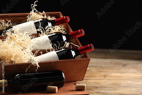 Box with wine bottles on wooden table against black background. Space for text