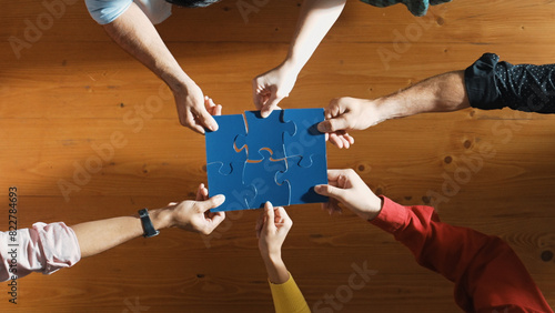 Top down view of skilled business people assemble blue jigsaw puzzle on meeting table. Group of diverse team working together to solve the puzzle. Represented togetherness, cooperative. Convocation.