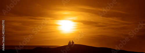 back, rear view of young Couple watching sunset at beach. man and woman sitting on coast at sunrays. horizon line above Black Sea.