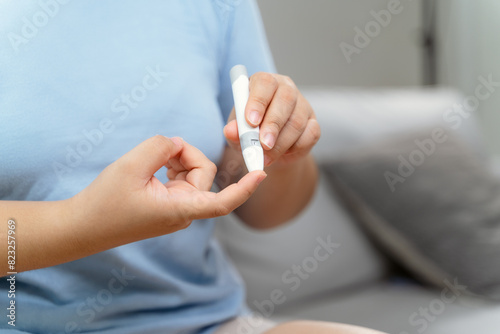 Asian woman using lancet on finger for checking blood sugar level by Glucose meter