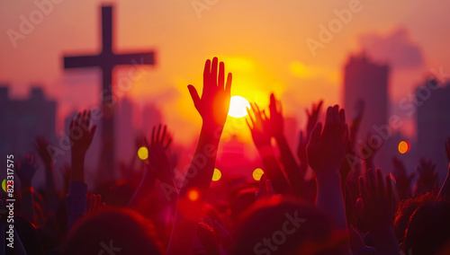 People raising hands in worship at sunset with city silhouette and cross