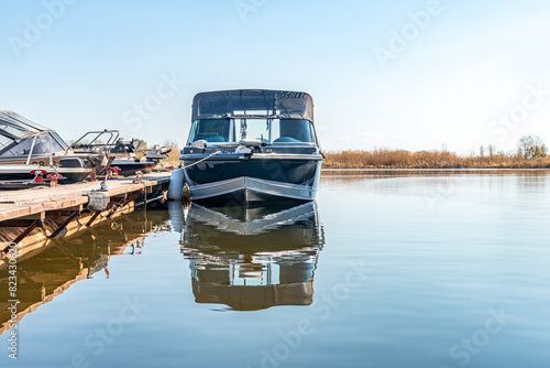Fishing boats moored at wooden pontoon pier in early morning. Modern motorboats in small docks on calm river. Ships in lake port on spring day