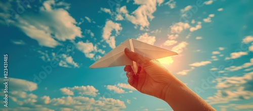 Hand holding a paper airplane against a sky background