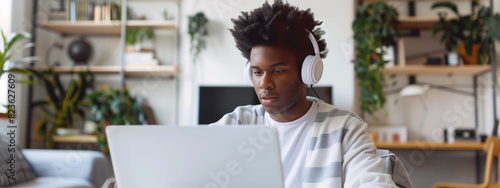 Young African American man immersed in online learning, his headphones and rapt expression reflecting a profound engagement with the digital world In cosy bedroom setting