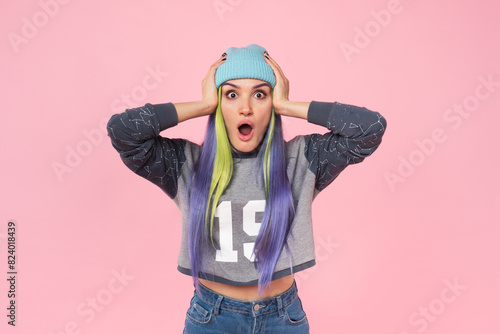 Excited happy cheerful young caucasian woman teenage girl hipster with dyed colorful hair looking at camera touching her head with shock impression isolated in pink background