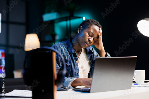 A weary and agitated black woman is staring at her wireless computer on the table. Exhausted African American female entrepreneur reading online research papers on a digital laptop.