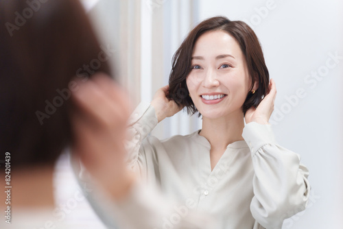 鏡を見て髪の毛を触るミドル女性（美容・ヘアセット・ヘアケア・髪の毛）