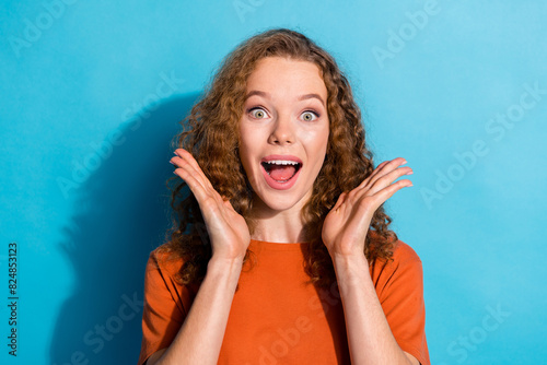 Photo portrait of youth beautiful funny girl with wavy hair wear orange t shirt raised hands up surprised isolated on blue color background