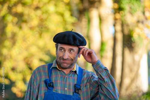 Portrait of a Frenchman, wearing a beret and blue dungarees smiling and gesticulating to camera