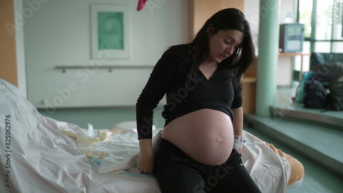 Pregnant woman suffering from contractions during pre labor at clinic covering face in pain, expecting mother at hospital waiting for childbirth