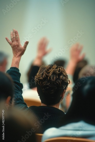 A group of people are sitting in a room and one person is raising their hand. Scene is one of anticipation or excitement, as the person is likely waiting for something important to happen