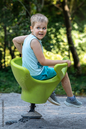 Portrait of surprised smiling boy in park playground on green spring-loaded plastic chair